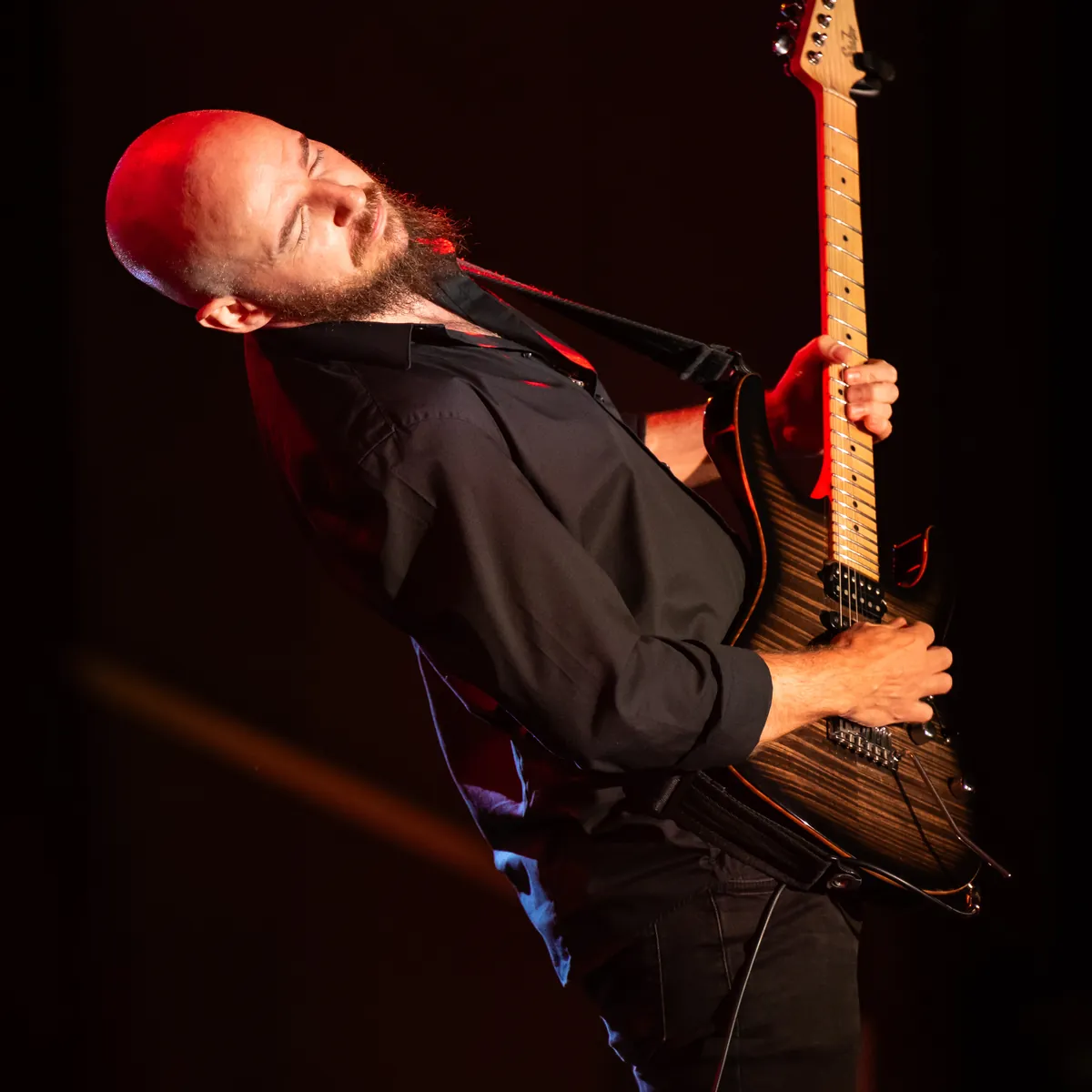 Ben Hartwell leaning back mid-solo with his electric guitar under red stage light